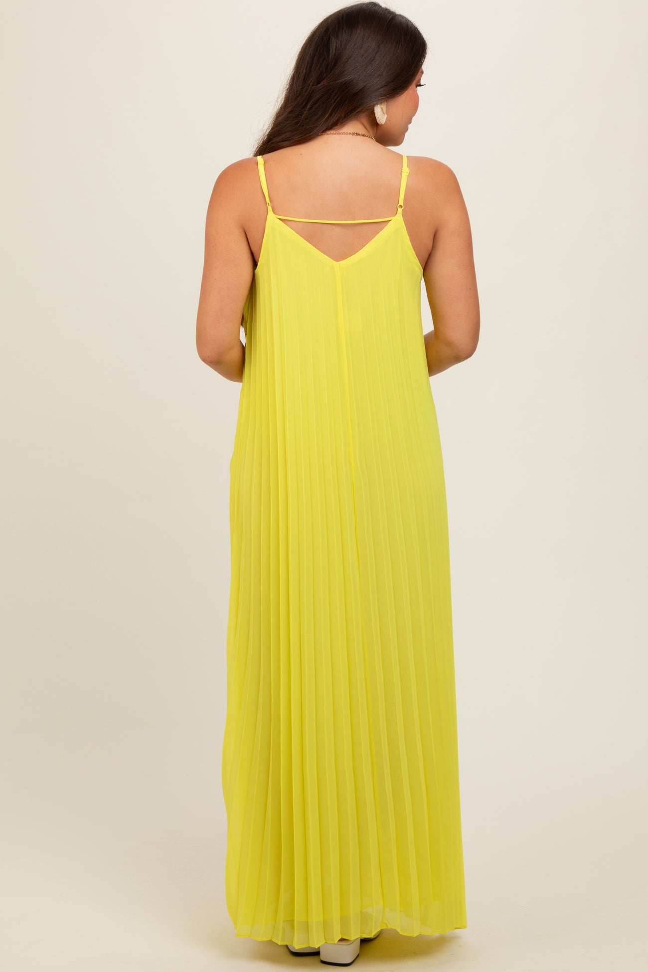 woman wearing a long yellow pleated maternity dress with adjustable straps, showing the back view and flowing silhouette