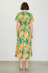 woman wearing a colorful floral midi dress with puffy sleeves and an elastic waist, standing with her back to the camera