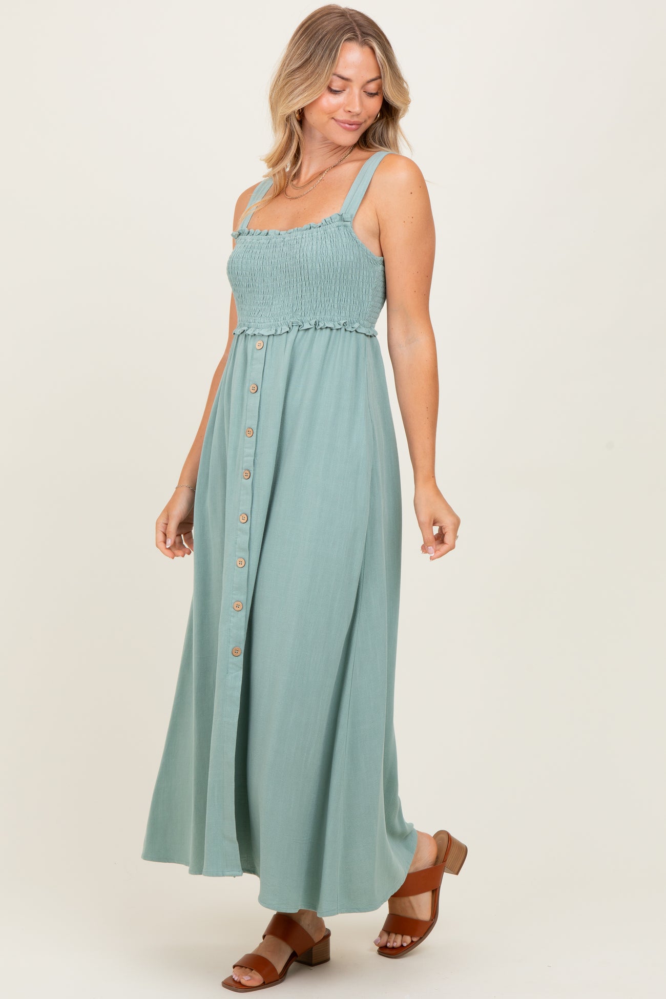 woman wearing a teal smocked maxi dress with adjustable straps and button detail, styled with brown heeled sandals