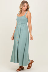 woman wearing a teal smocked maxi dress with adjustable straps and button detail, styled with brown heeled sandals