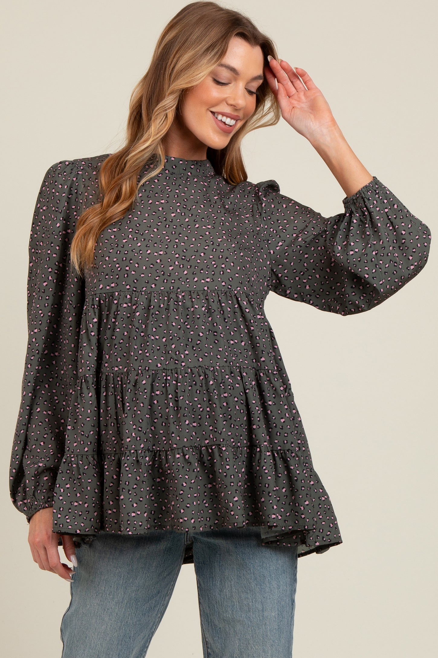 woman wearing a gray maternity top with a tiered ruffle design and long puff sleeves, smiling and posing