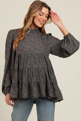 woman wearing a gray maternity top with a tiered ruffle design and long puff sleeves, smiling and posing