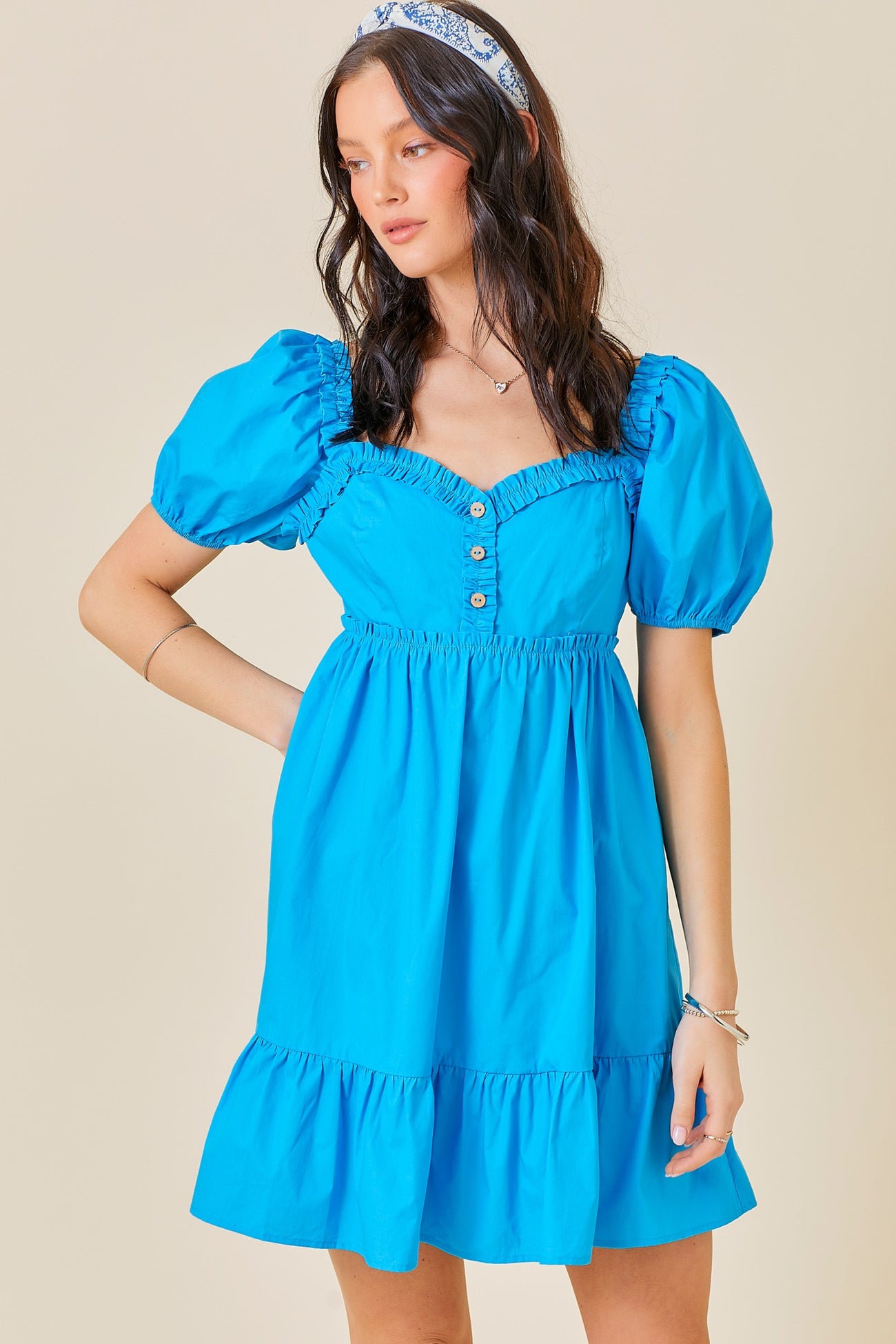 woman wearing a bright blue puff sleeve mini dress with a ruffled hem and button details