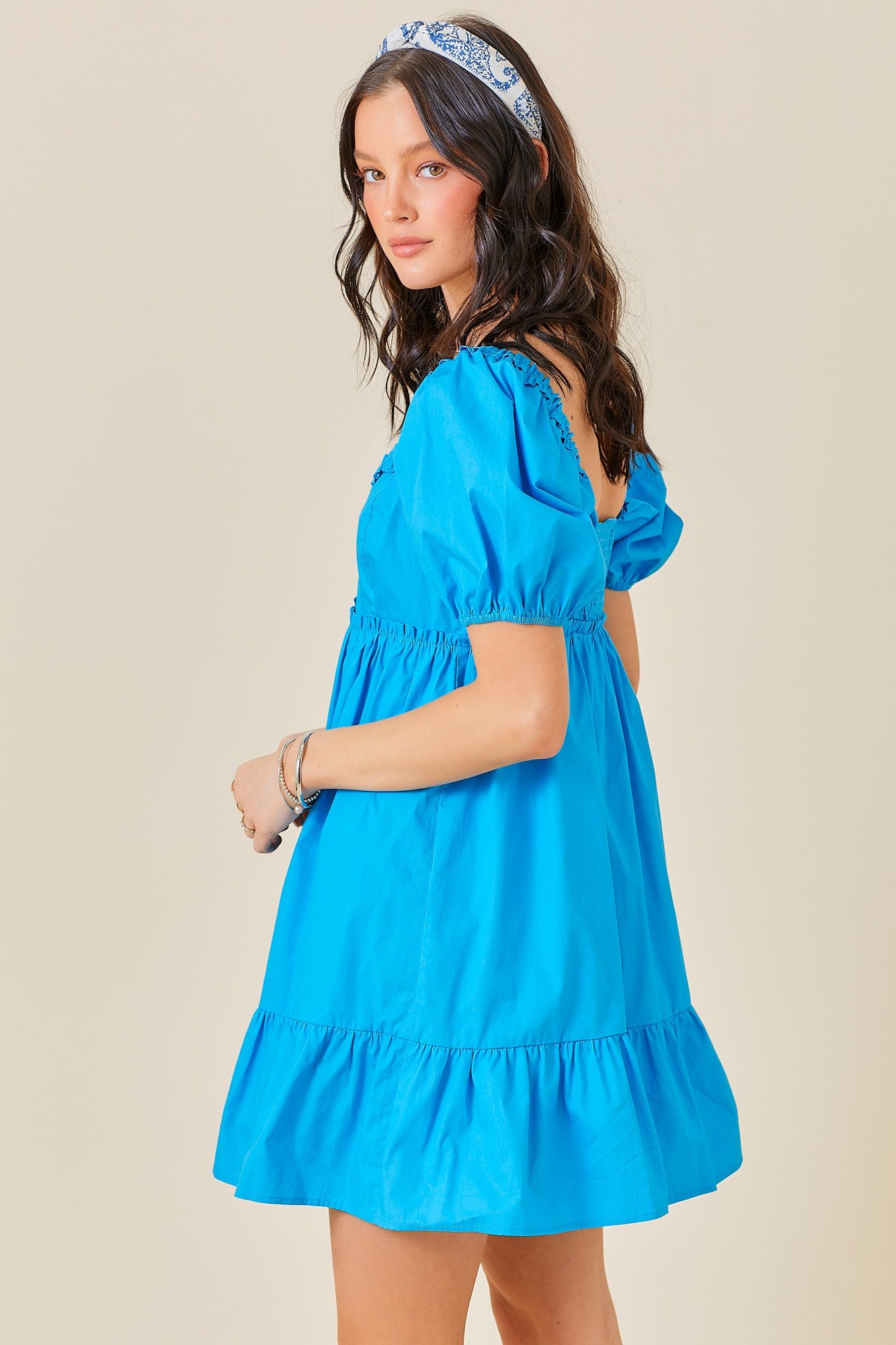 woman wearing a bright blue puff sleeve mini dress with a ruffled hem and an open back