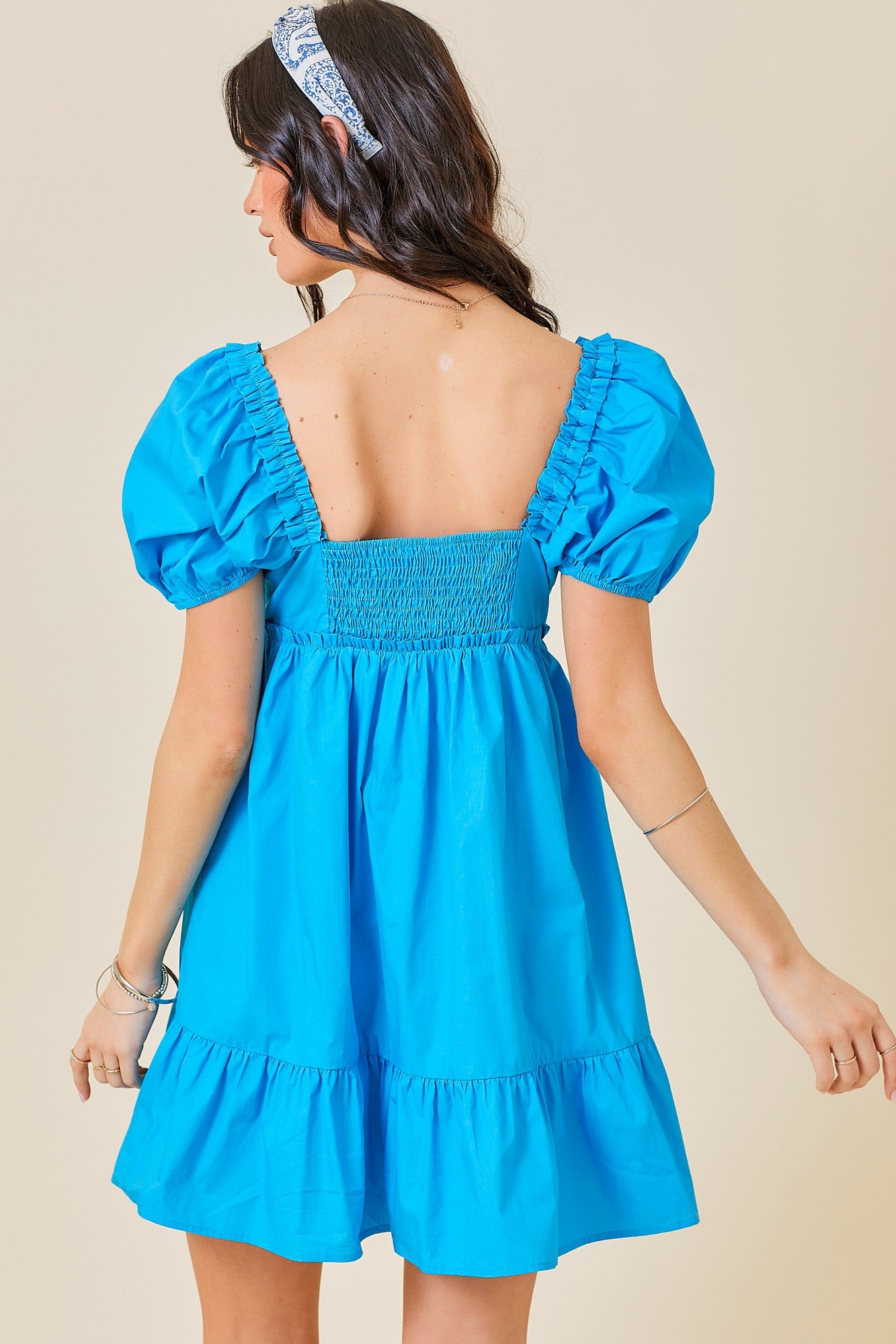 woman wearing a bright blue puff sleeve mini dress with a back smocked design and tiered ruffle hem