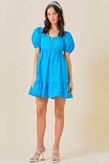 woman wearing a bright blue puff sleeve mini dress with a button detail and tiered skirt