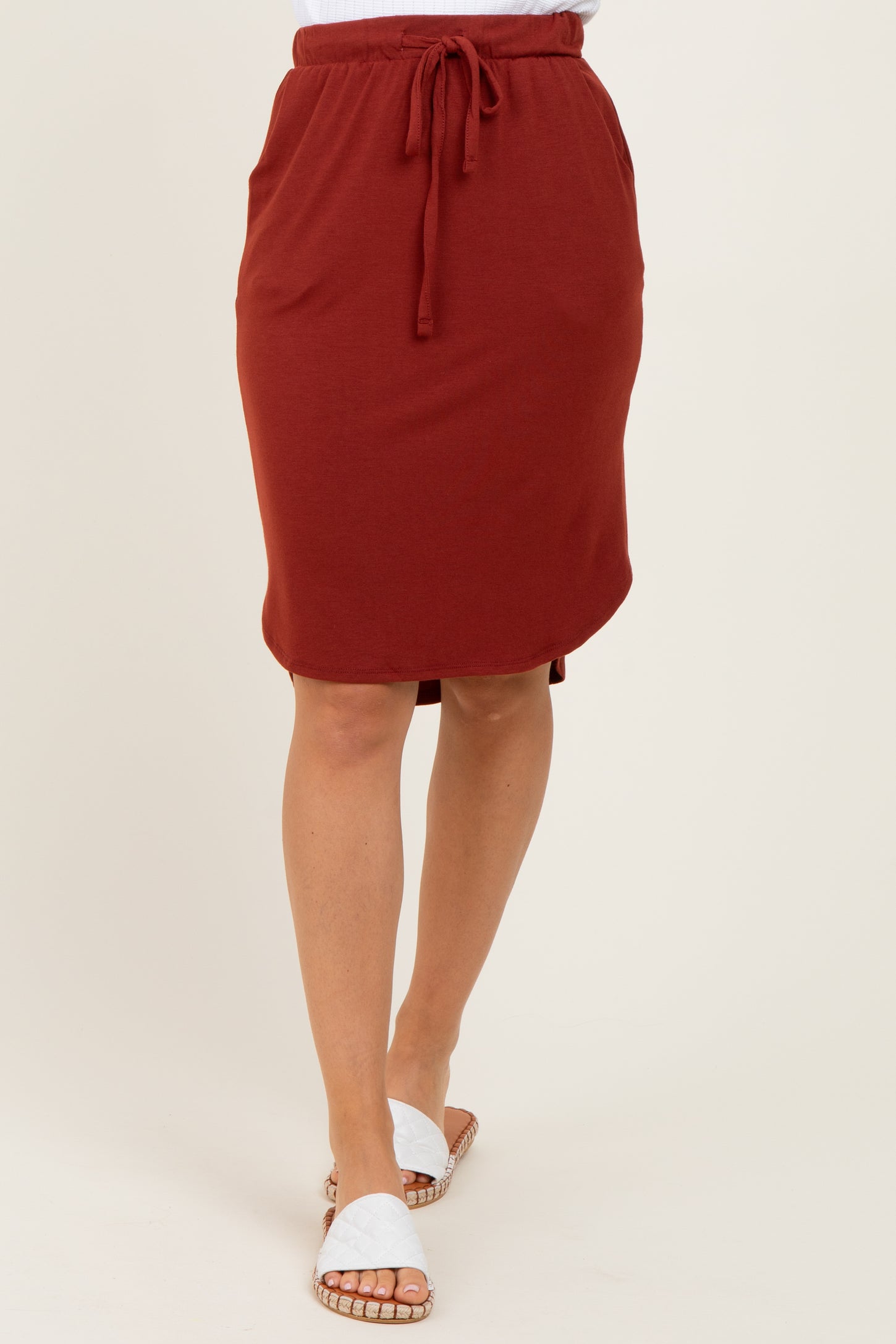 woman wearing a rust colored knee-length skirt with a drawstring waist and side pockets, paired with flat sandals