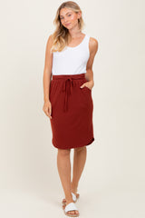 woman wearing a white ribbed tank top and a rust-colored drawstring skirt, standing in a relaxed pose