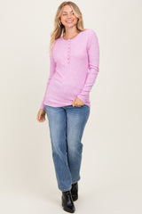 woman wearing a pink long sleeve ribbed henley top and blue jeans, smiling and standing against a neutral background