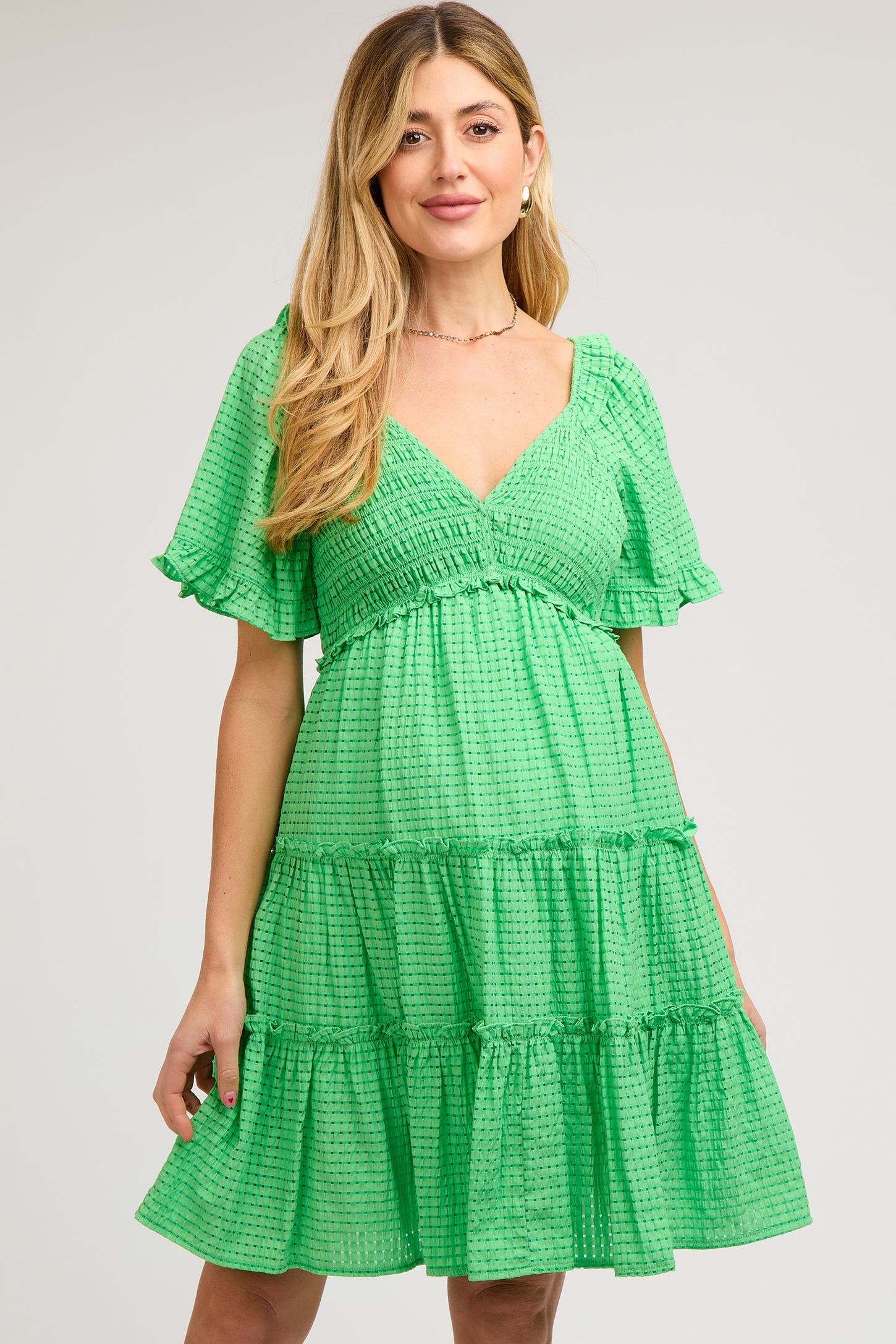 woman wearing a green smocked maternity dress with flutter sleeves and tiered ruffles, showcasing her baby bump