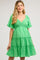 woman wearing a green smocked maternity dress with flutter sleeves and tiered ruffles, showcasing her baby bump