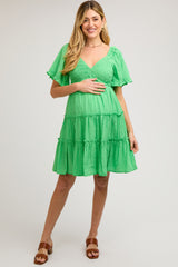 woman wearing a green tiered maternity dress with short ruffled sleeves and holding her baby bump