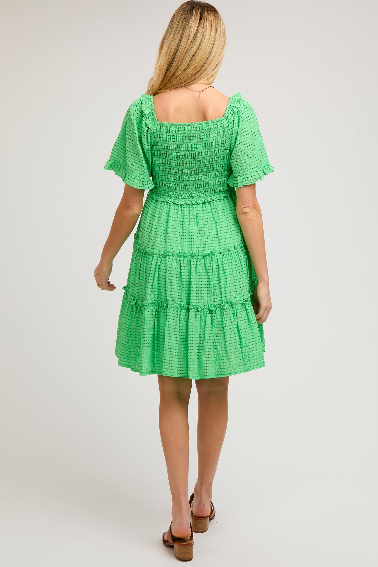 woman wearing a green maternity dress with a tiered skirt and puff sleeves, viewed from the back