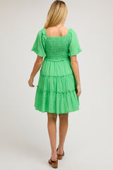 woman wearing a green maternity dress with a tiered skirt and puff sleeves, viewed from the back