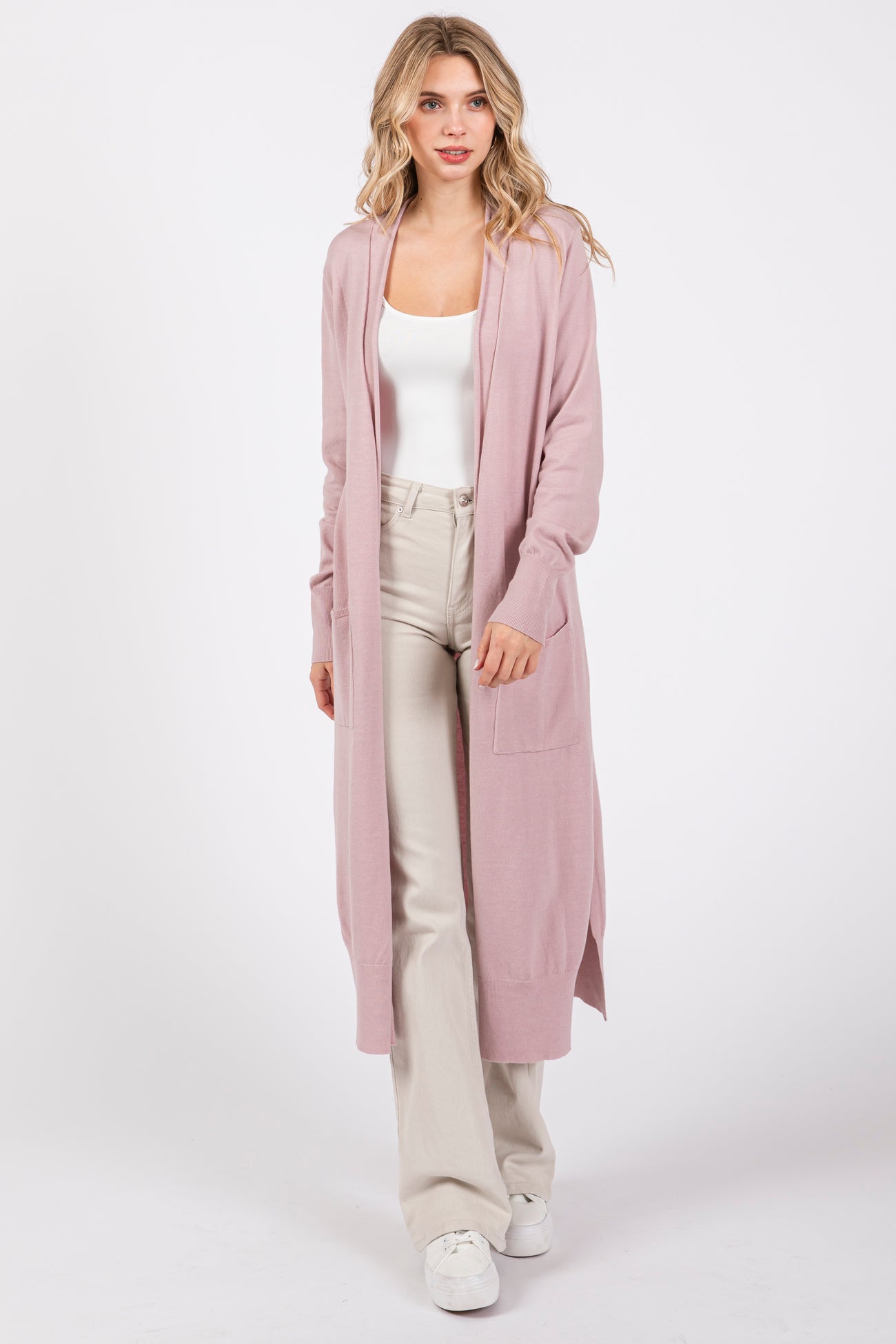 woman wearing a light pink long cardigan with pockets, paired with a white tank top and cream wide-leg pants