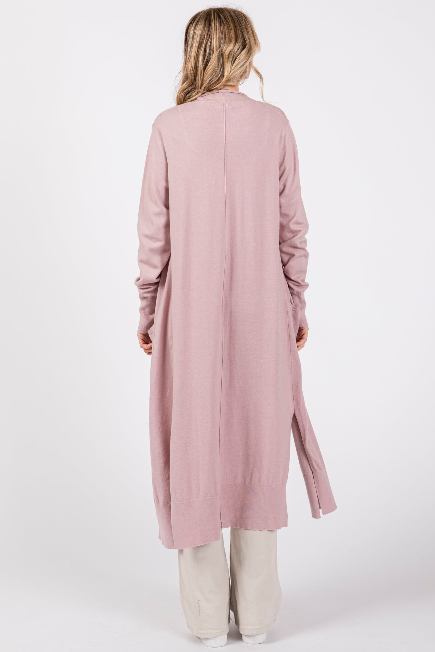 woman wearing a long sleeve light pink cardigan with a side slit, shown from the back