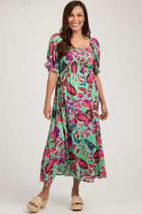 woman wearing a colorful floral print maternity dress with puff sleeves and a smocked bodice, featuring a flowy skirt