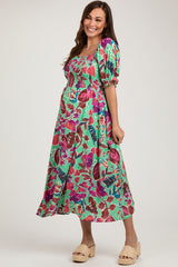 woman wearing a green floral maternity dress with puff sleeves and a fitted bodice, showing her baby bump