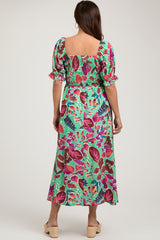 woman wearing a green maternity maxi dress with colorful floral print and puff sleeves, showing her baby bump from the back