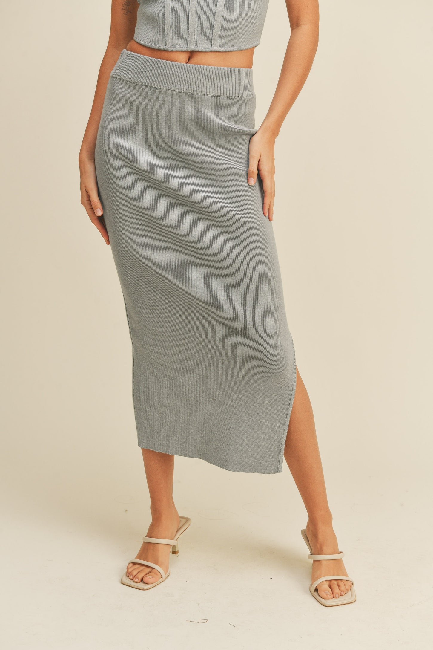 woman wearing a light gray ribbed midi skirt with a side slit and matching crop top