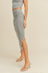 woman wearing a gray ribbed midi skirt with a side slit and a matching crop top, paired with strappy heels