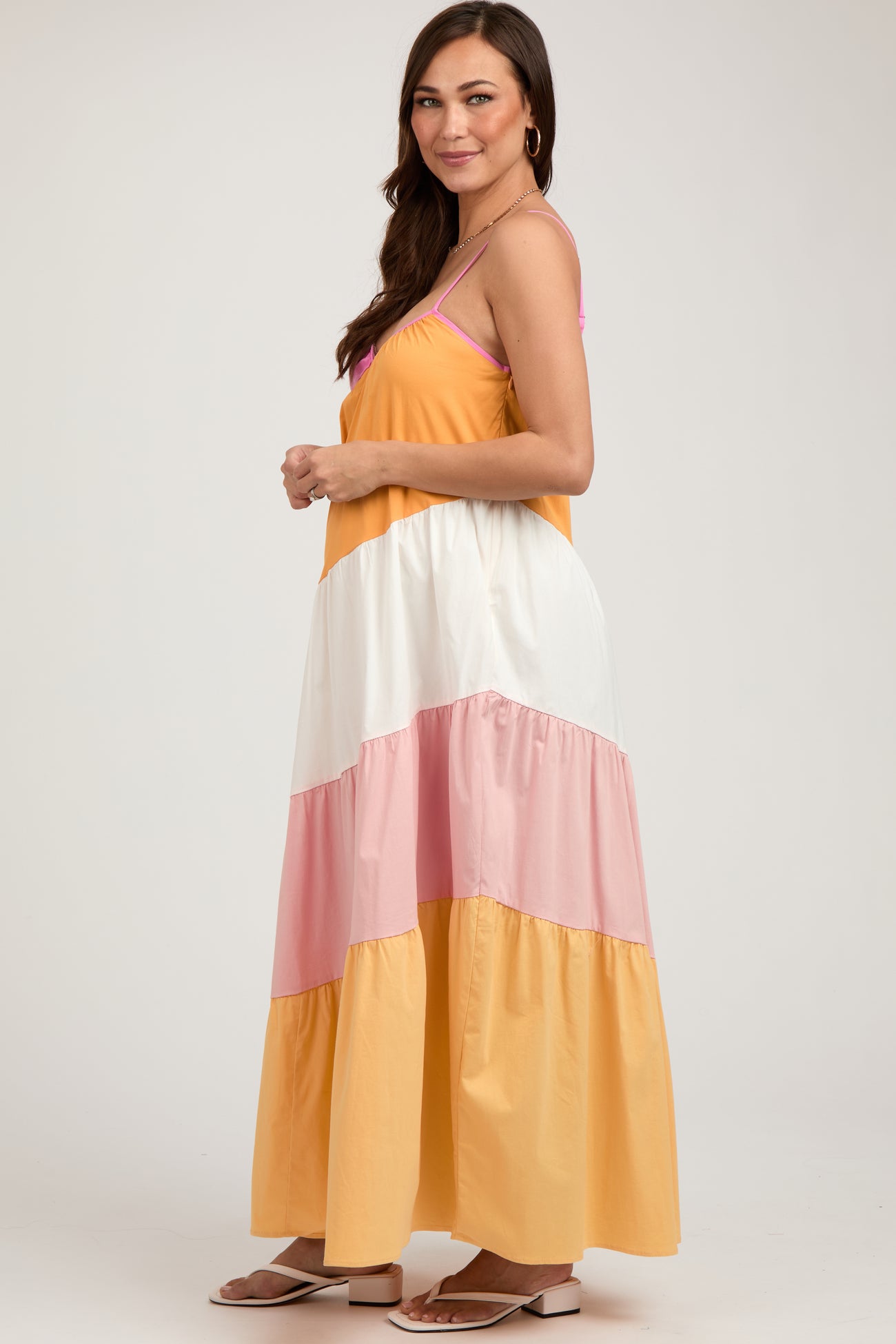 woman wearing a colorful maternity maxi dress with yellow, white, and pink tiers, showcasing her baby bump