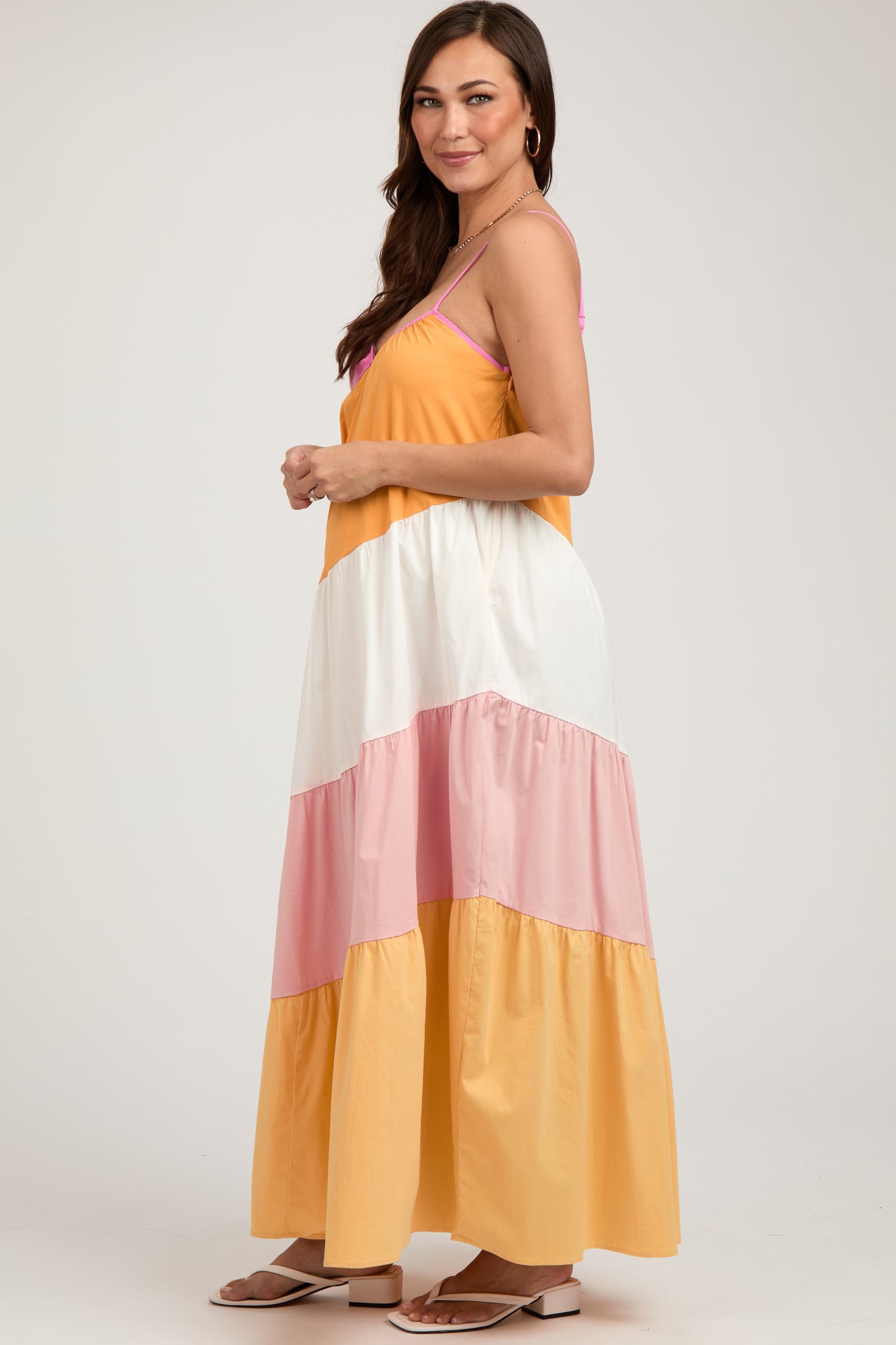 woman wearing a colorful maternity maxi dress with yellow, white, and pink tiers, showcasing her baby bump