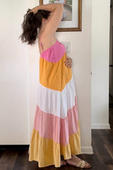 woman wearing a maternity color block maxi dress with pink, white, yellow, and peach panels, holding her baby bump