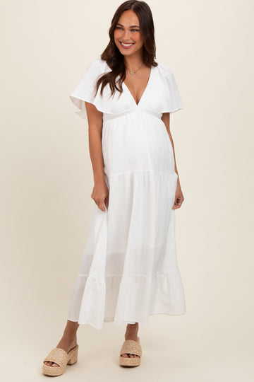 woman wearing a white maternity maxi dress with flutter sleeves and a fitted bodice displaying her baby bump