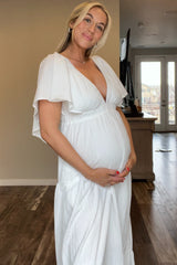 woman wearing a white maternity dress with flutter sleeves and holding her baby bump