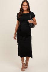 woman wearing a black short sleeve maternity dress with side ruching, holding a black handbag, and showing her baby bump