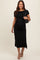 woman wearing a black short sleeve maternity dress with side ruching, holding a black handbag, and showing her baby bump
