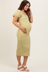 woman wearing a light green maternity dress with puff sleeves and a fitted skirt, cradling her baby bump