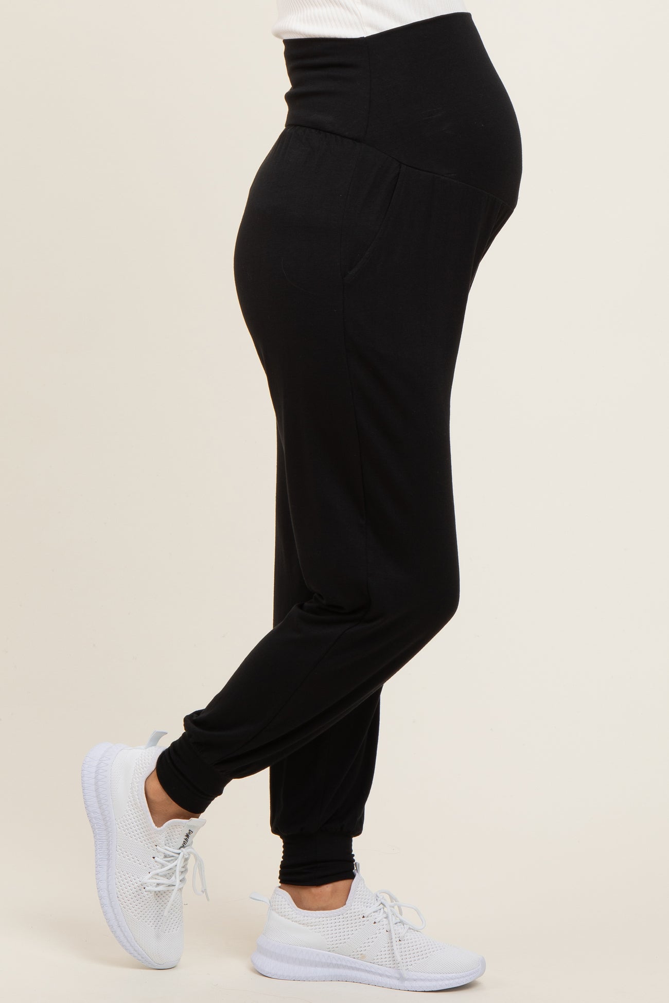 woman wearing black maternity joggers with a visible baby bump and white sneakers