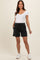 woman wearing a white short sleeve scoop neck top and black maternity shorts with an elastic waistband