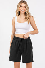 woman wearing a white ribbed crop top and black drawstring shorts, smiling at the camera