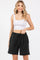 woman wearing a white ribbed crop top and black drawstring shorts, smiling at the camera