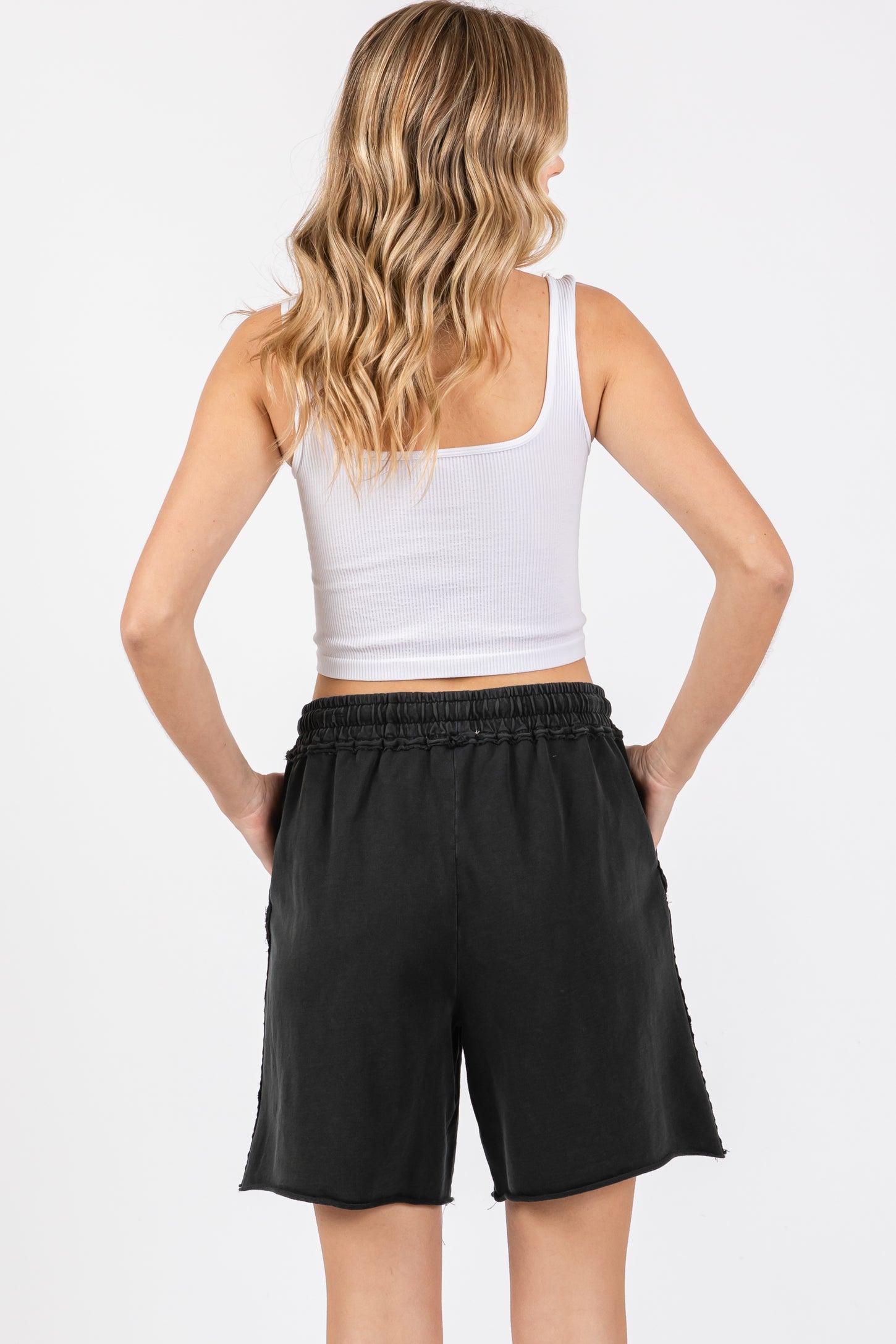 woman wearing a white tank top and black shorts, showing the back view of the outfit