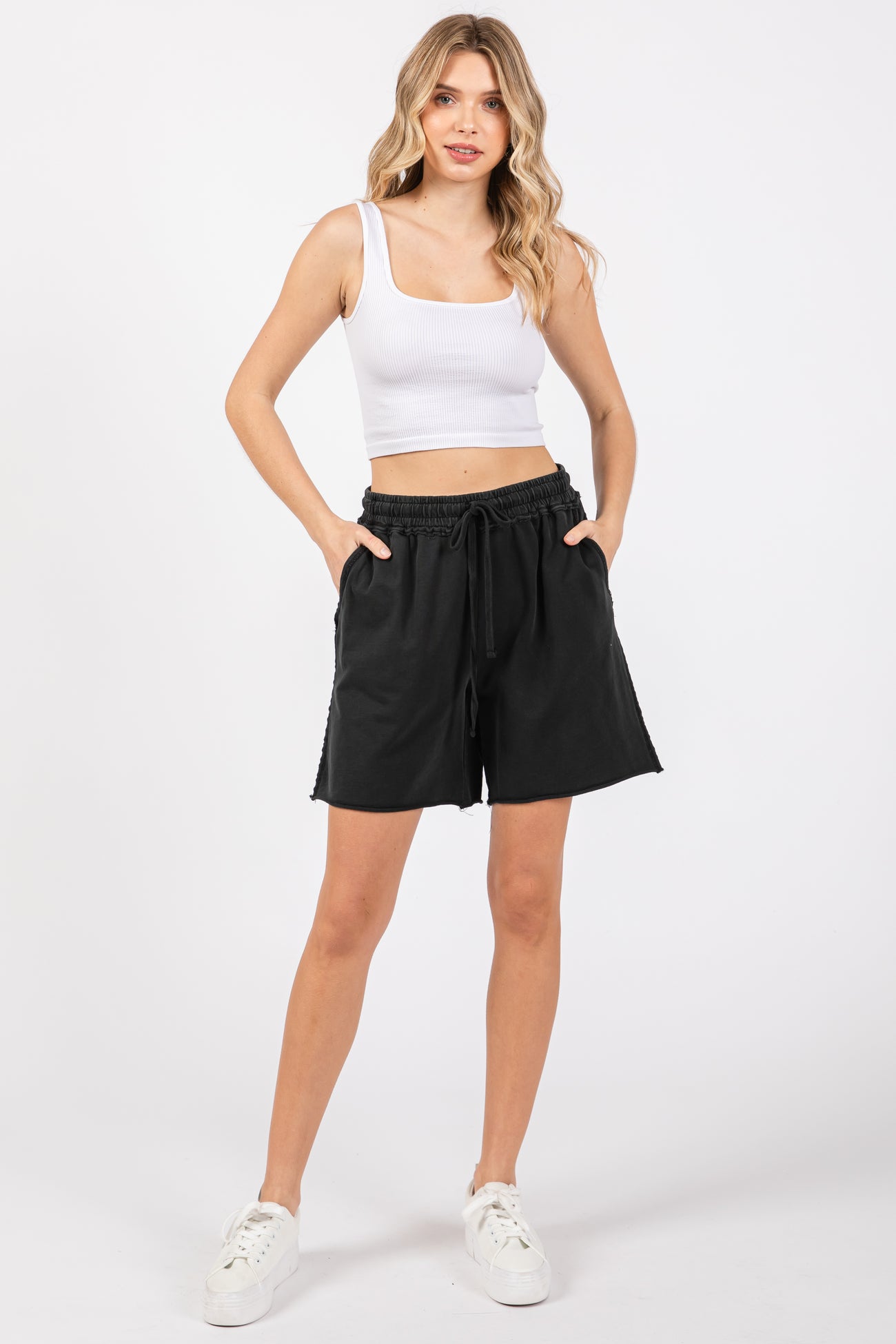 woman wearing a white fitted crop top and black drawstring shorts with pockets
