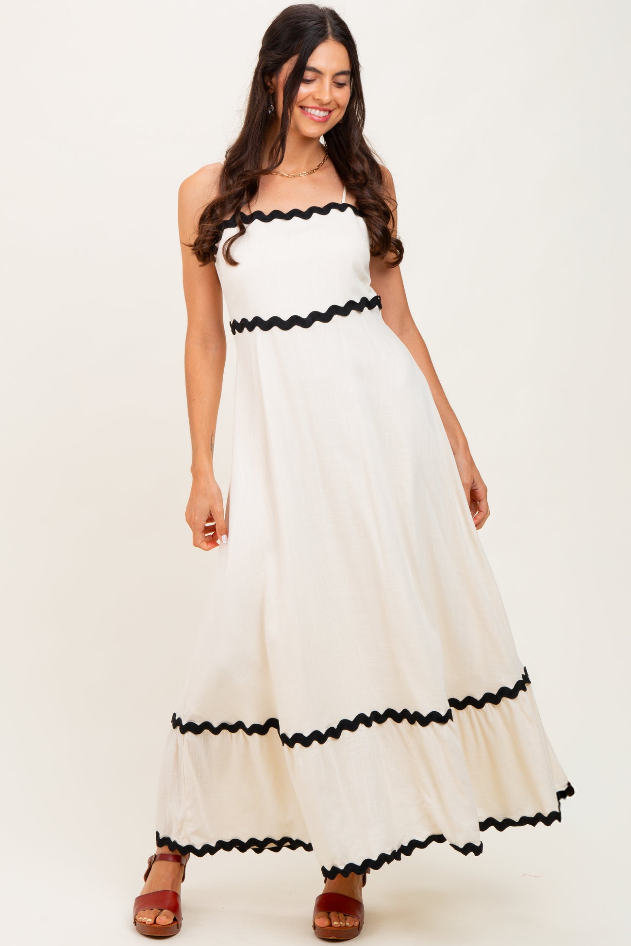woman wearing a white maxi dress with black ruffle trim and spaghetti straps, standing and smiling