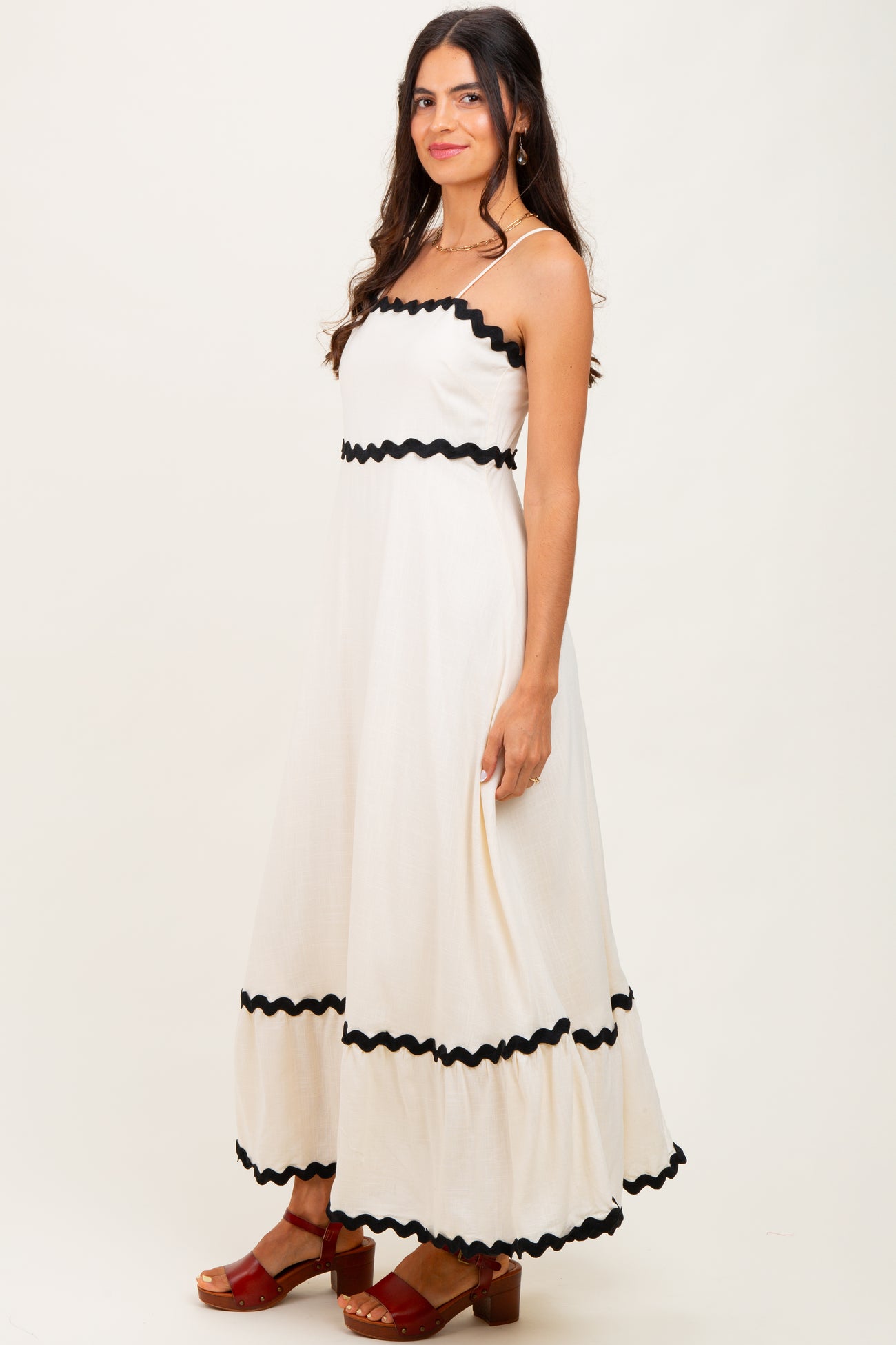 woman wearing a cream maxi dress with black ruffles and sandals, standing sideways against a neutral background