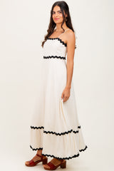 woman wearing a cream maxi dress with black ruffles and sandals, standing sideways against a neutral background