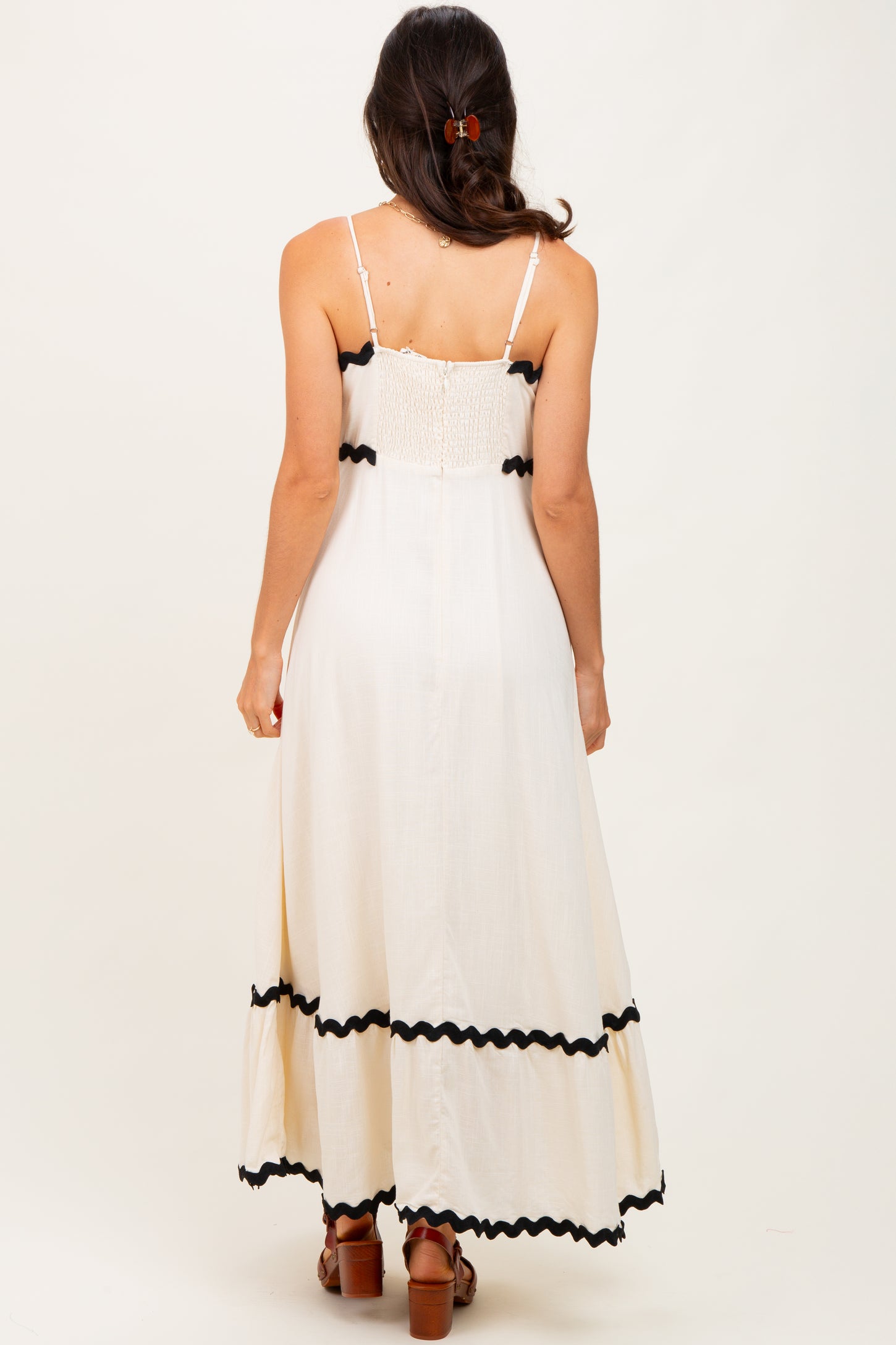 woman wearing a white maxi dress with black trim and spaghetti straps, shown from the back