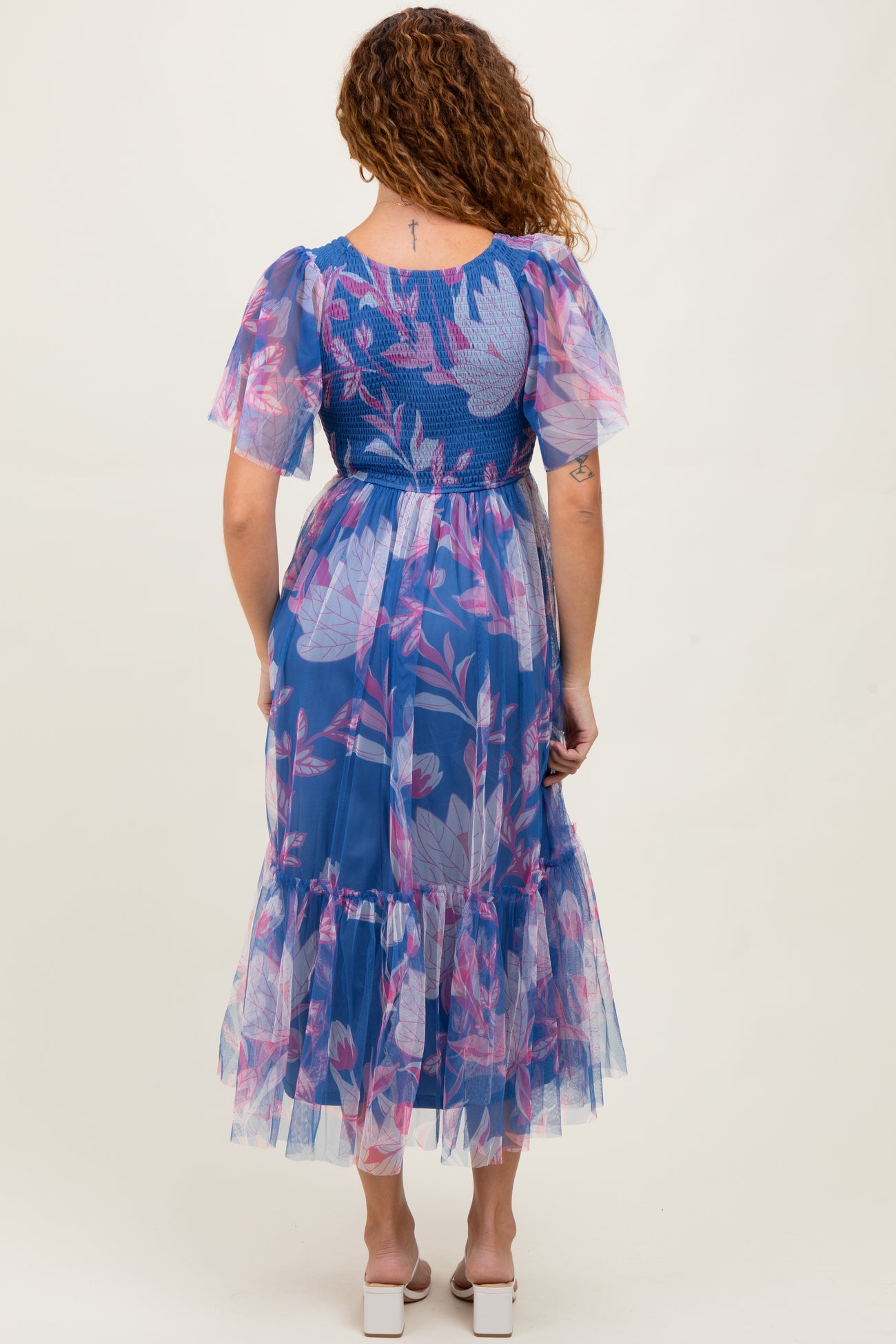 woman wearing a sheer blue floral maxi dress with puff sleeves and a ruffled hem, seen from the back