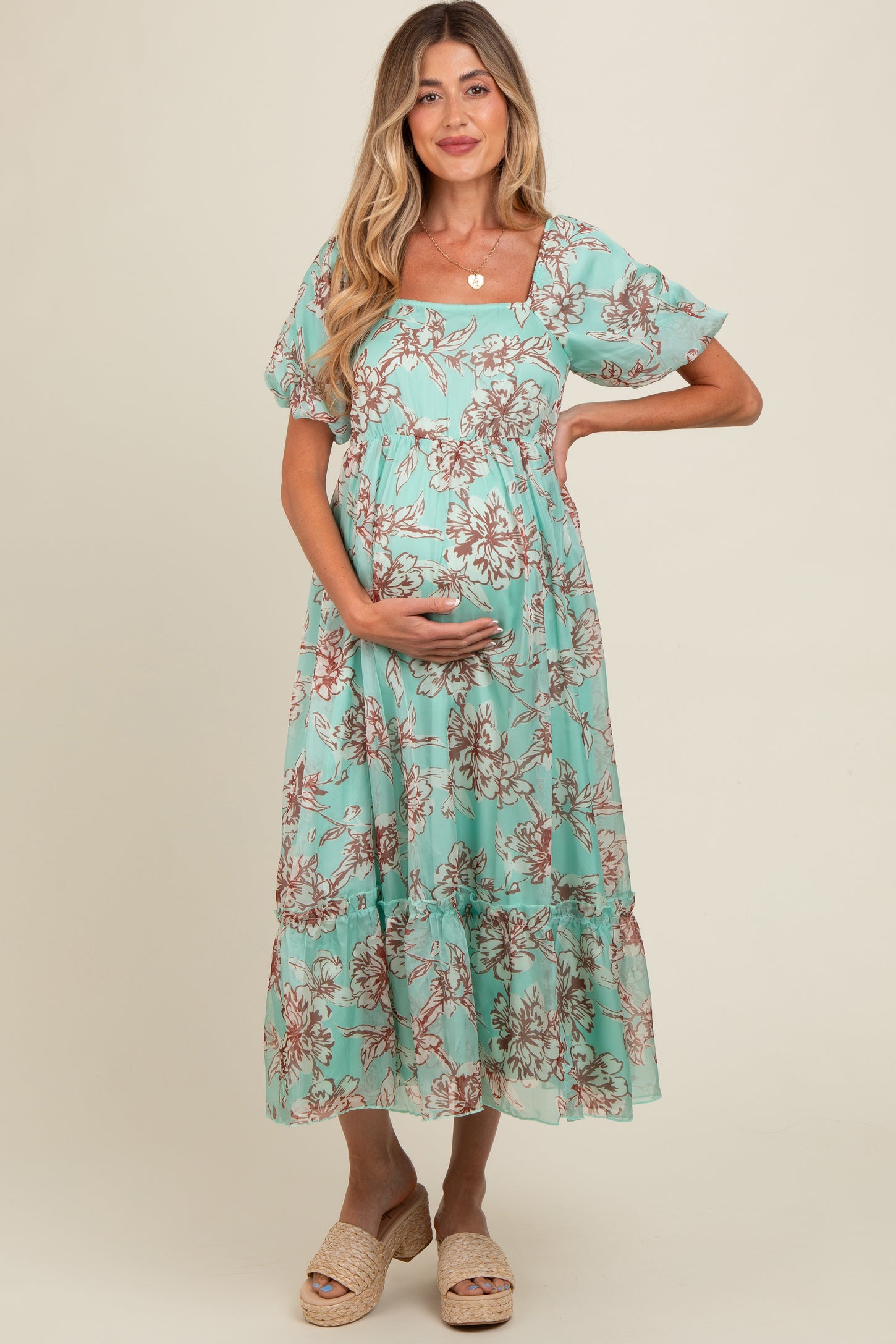 woman wearing a mint green floral maternity dress and holding her baby bump