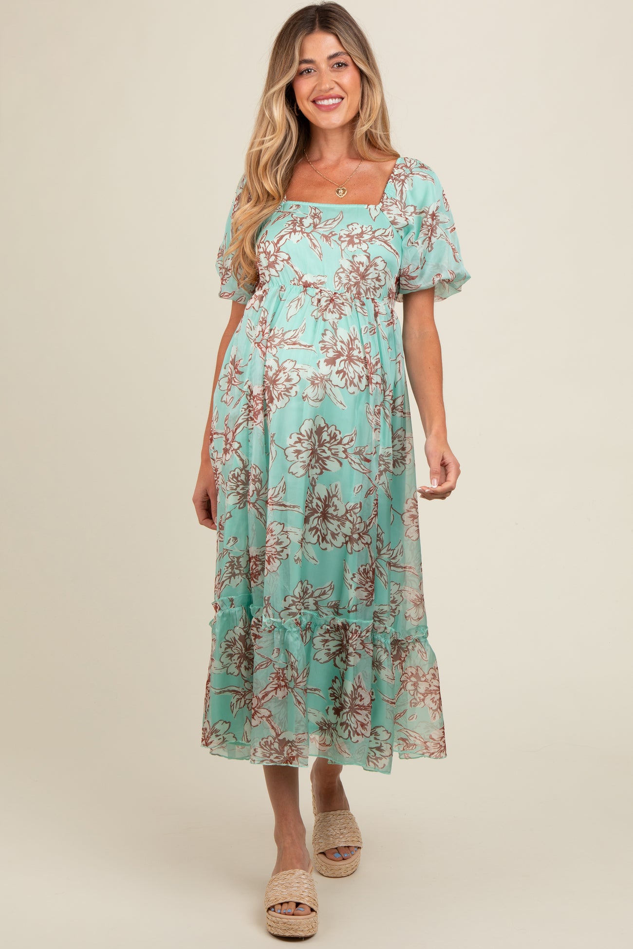 woman wearing a light teal floral maternity dress with puff sleeves and ruffled hem, showcasing her baby bump