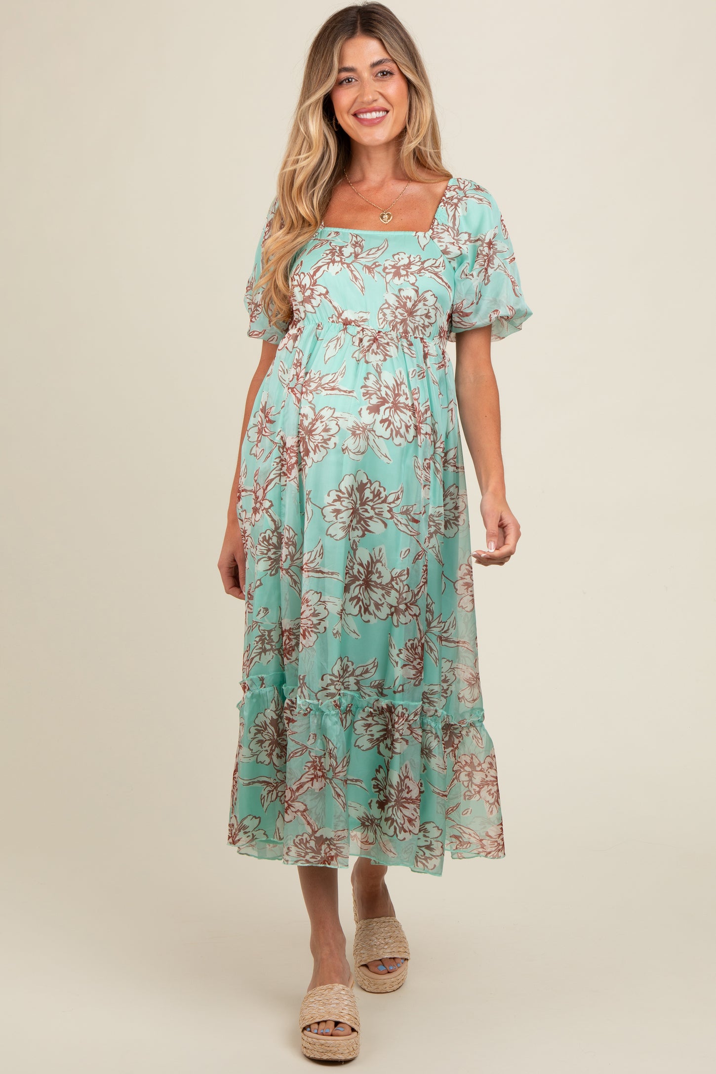 woman wearing a light teal floral maternity dress with puff sleeves and ruffled hem, showcasing her baby bump