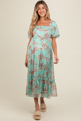 woman wearing a light teal floral maternity dress with puff sleeves and ruffled hem, showcasing her baby bump