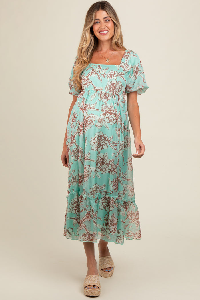woman wearing a light teal floral maternity dress with puff sleeves and ruffled hem, showcasing her baby bump