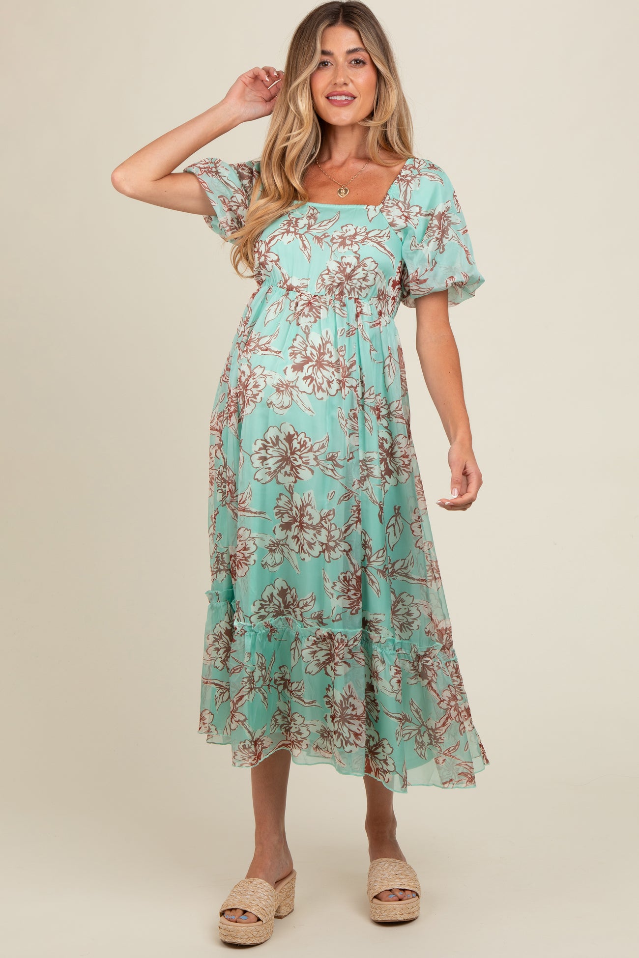 woman wearing a mint green floral maternity dress with short sleeves and a tiered skirt, showing her baby bump